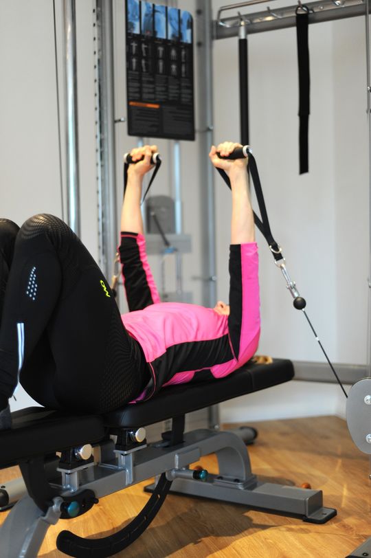 Frau trainiert auf Langbank mit Seilen im modernen Fitnessraum